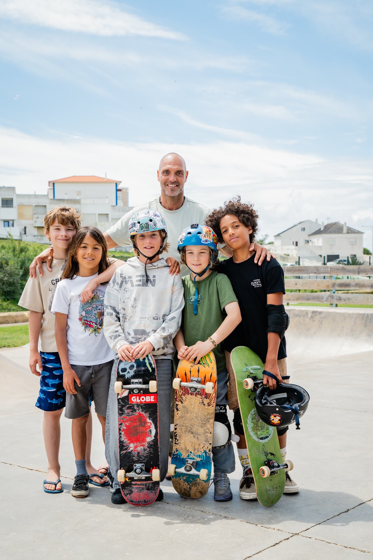 Un coach se tient avec cinq garçons tenant leurs skateboards au skatepark